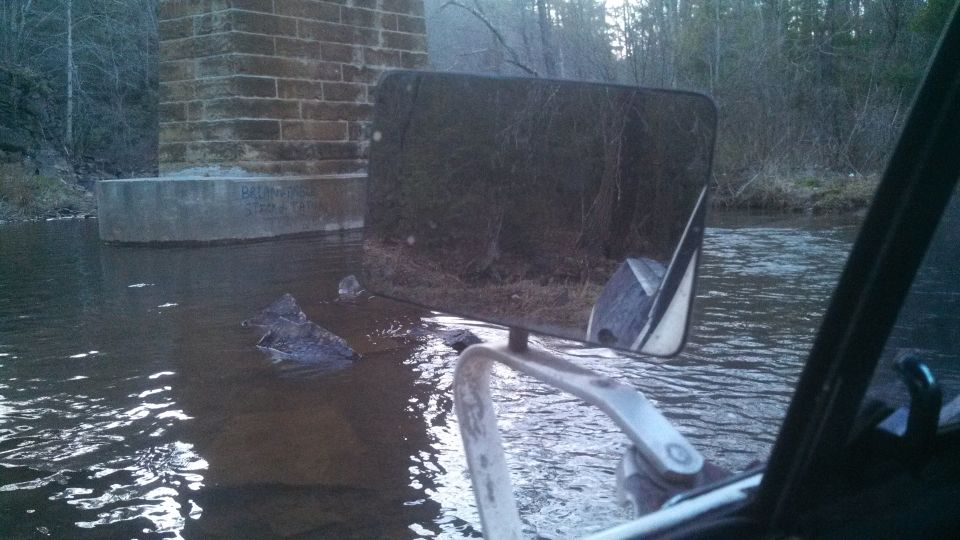 Ford Bronco partially submerged in water, viewed from interior, showing side mirror and reflection of trees