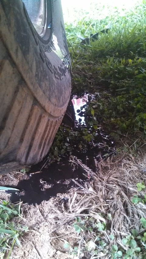 1979 Ford Bronco - A close-up view of a tire resting near a puddle of liquid on the ground.