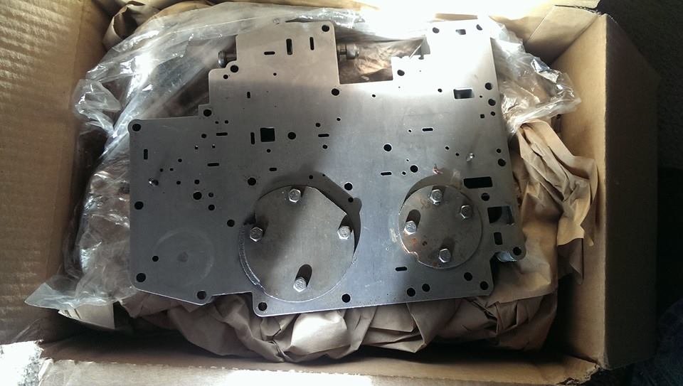Metal plate with circular indentations and bolts, inside a cardboard box