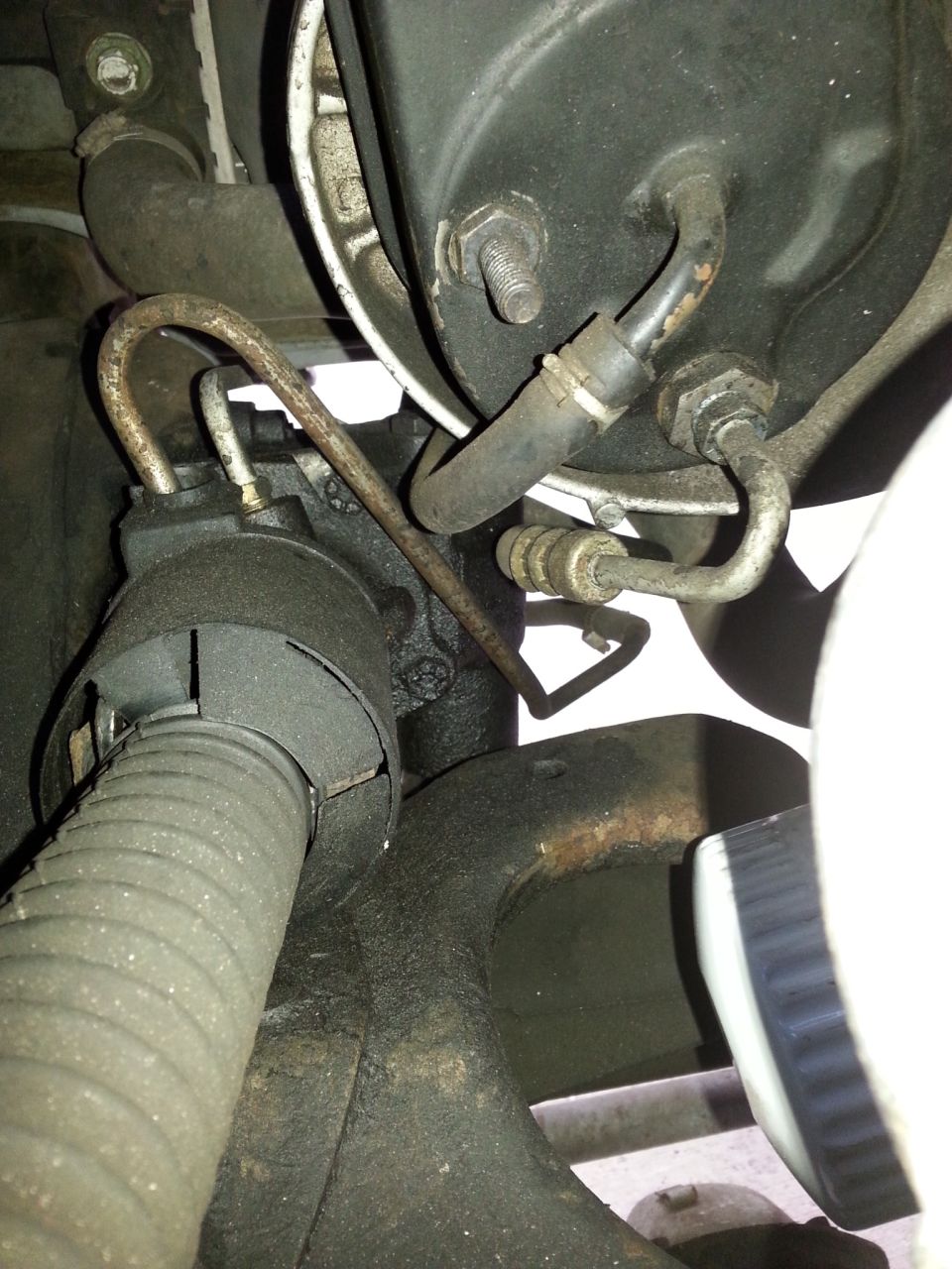 Close-up of a greasy power steering pump with metal hoses and a ribbed rubber hose