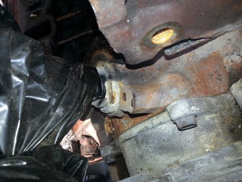 1994 Ford Bronco - Detail of a heavily corroded engine block and exhaust manifold, partially obscured by black plastic sheeting.