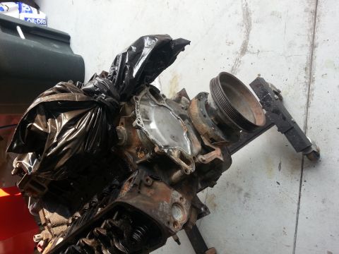 1994 Ford Bronco - Engine block with a plastic bag covering part of it, leaning against a concrete wall.