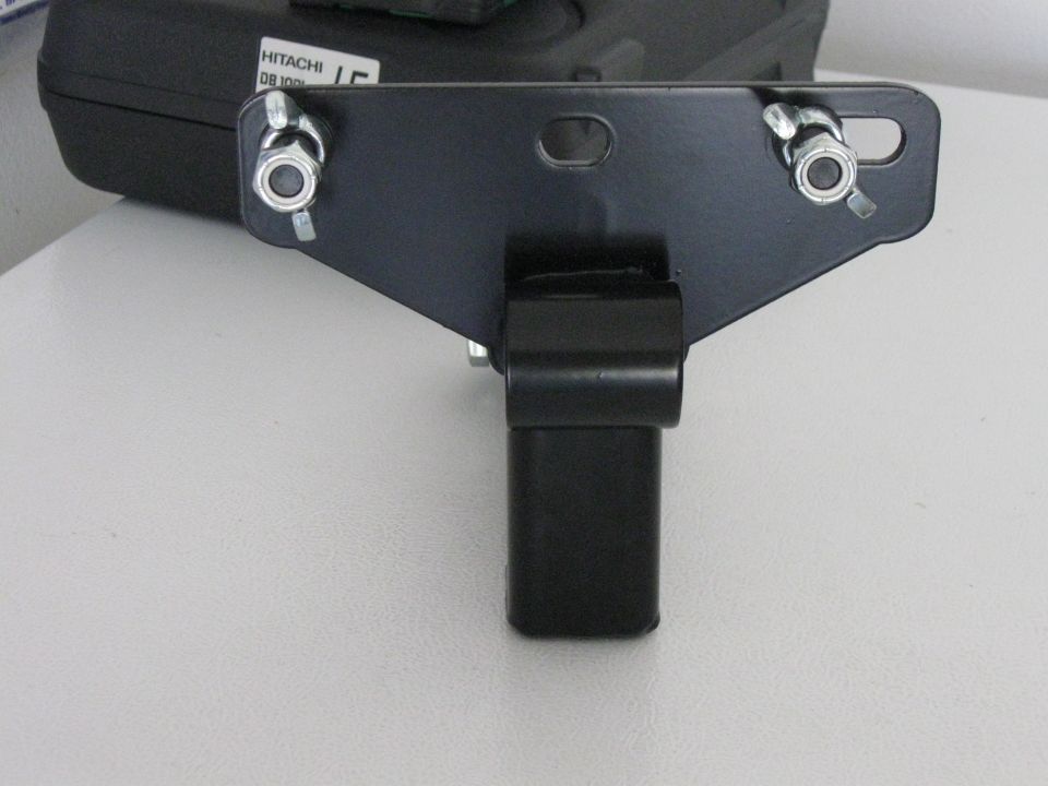 Black metal hitch receiver part with bolts and nuts, resting on a white surface. Hitachi logo visible on a black case in background