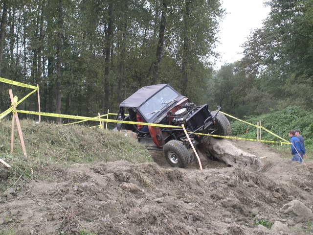 Red 1982 Ford Bronco climbing muddy hill, hood open