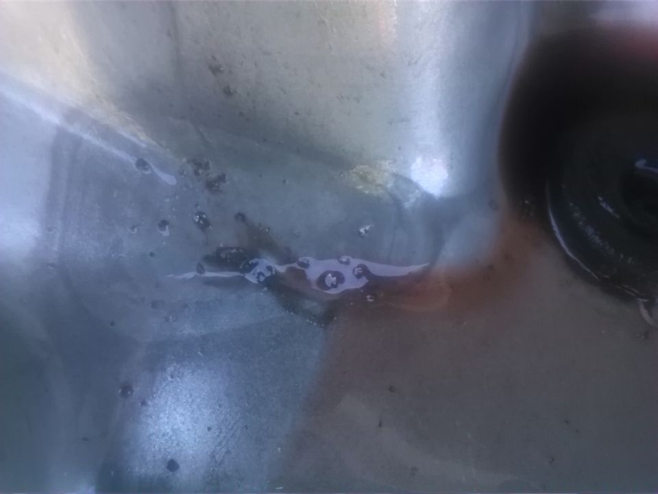 Close-up of a dirty engine oil pan with some fluid residue