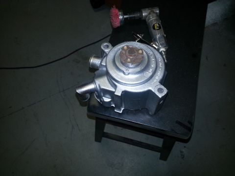 1994 Ford Bronco - A silver water pump is shown with an air tool and wire brush, resting on a black stool.