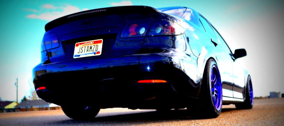 Dark blue sedan from rear, with custom blue wheels and a spoiler