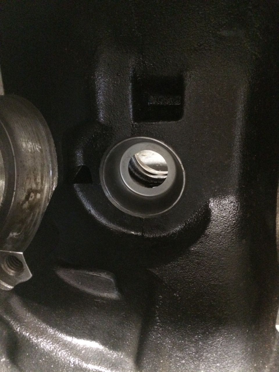 Black engine part with a circular opening and a bolt head visible