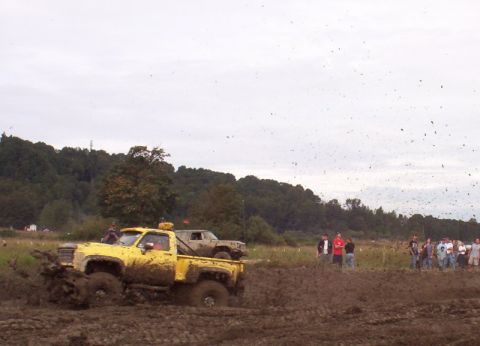 1982 Ford Bronco - A yellow pickup truck is stuck in the mud during a competition, with spectators watching in the background.