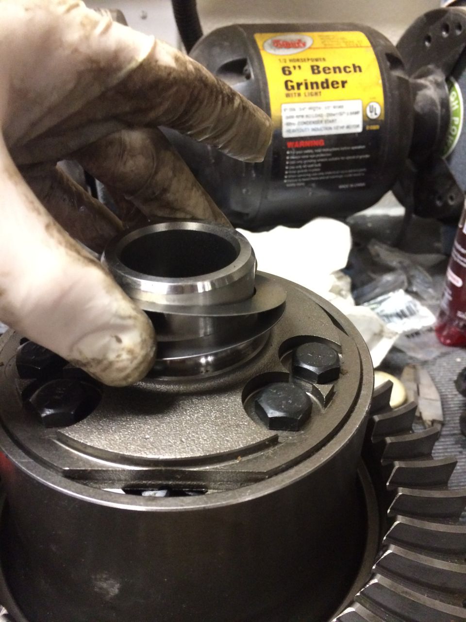 Hand fitting a bearing race onto a differential carrier near a 6-inch bench grinder