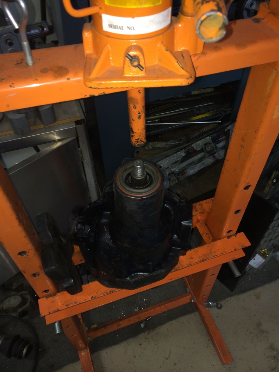 Black automotive differential housing and bearing assembly in an orange hydraulic press. Serial No. label visible on press