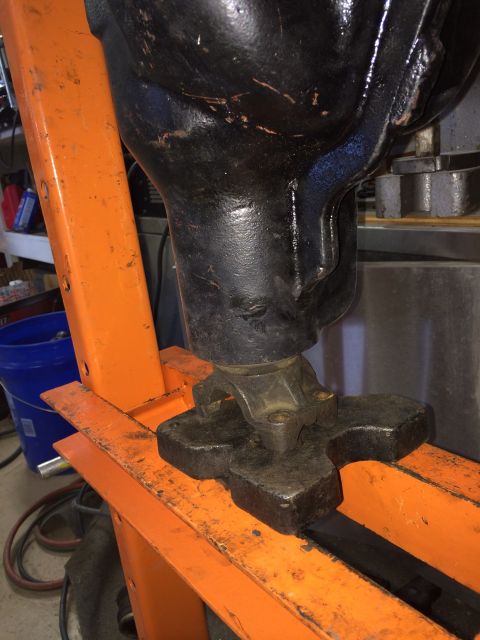 1996 Ford Bronco - A close-up view of a black u-joint assembly being pressed by an orange hydraulic press. The u-joint is attached to a black component, possi…