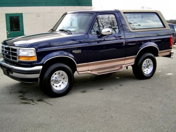 Dark blue Ford Bronco with tan two-tone trim and hardtop, front three-quarter view on wet pavement