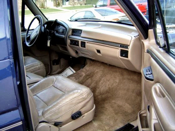 Tan leather interior and dash of a dark blue Ford Bronco viewed through open passenger door