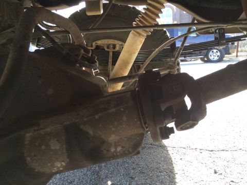 1996 Ford Bronco - Underside view of a vehicle's rear axle, driveshaft, leaf springs, and shock absorber. Another vehicle is visible in the background.