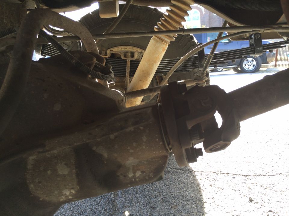 Close-up of driveshaft U-joint and rear suspension leaf springs. Another vehicle is visible in the background