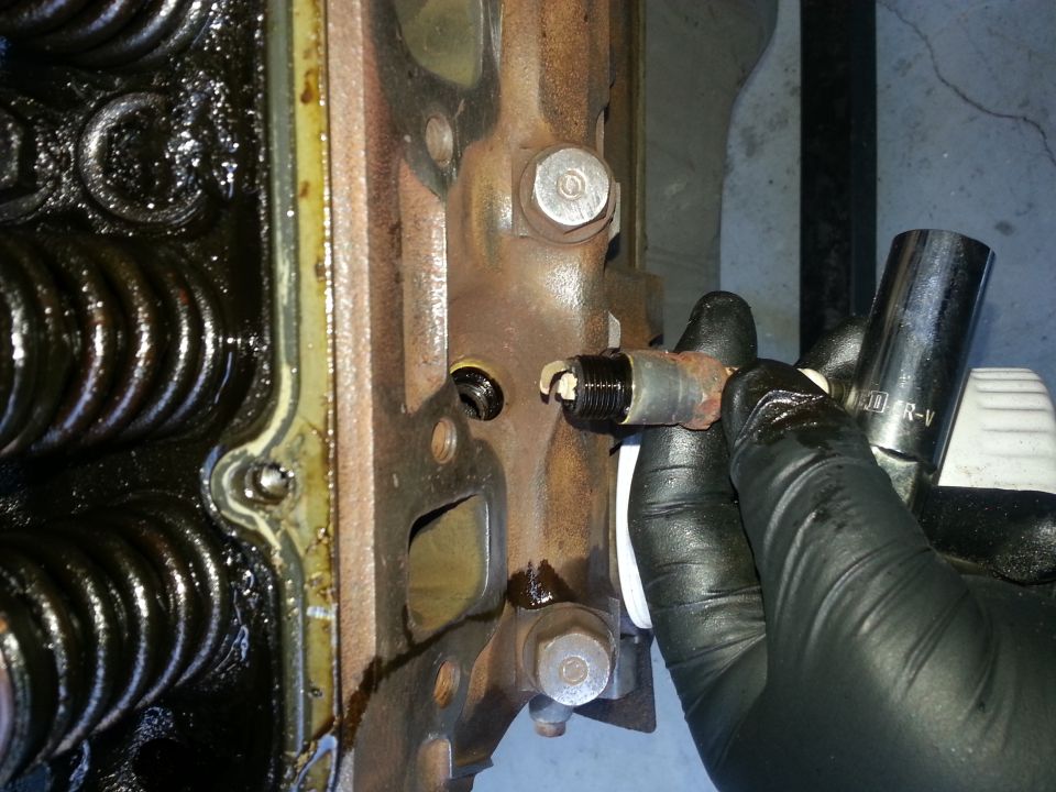 Gloved hand using a socket wrench to remove a spark plug from an engine block