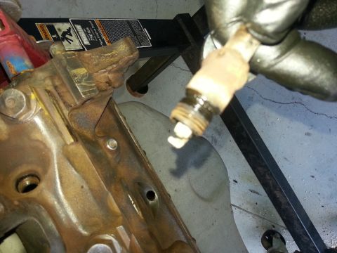 1994 Ford Bronco - A spark plug is held above a heavily rusted engine block, with the Supermotors.net logo in the lower right corner.