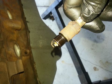 1994 Ford Bronco - A dirty spark plug is held near a rusty engine block, likely during a maintenance or repair task.