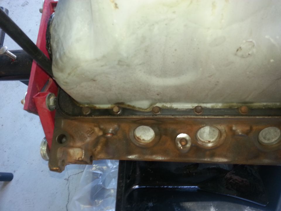 Engine oil pan with visible gasket and bolts, mounted on a red engine stand
