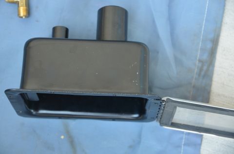 1979 Ford Bronco - A black metal part with two cylindrical protrusions and a hinged lid is shown against a blue background.