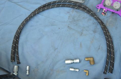 1979 Ford Bronco - Braided fuel lines and fittings are laid out on a blue surface, possibly for installation.