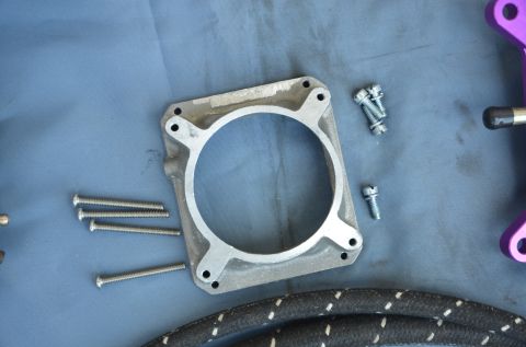 1979 Ford Bronco - A carburetor spacer and various screws are laid out on a blue surface, with the Supermotors logo visible at the bottom.