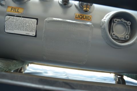 1979 Ford Bronco - A close-up view of a propane tank, showing its fill and liquid ports and a certification plate.