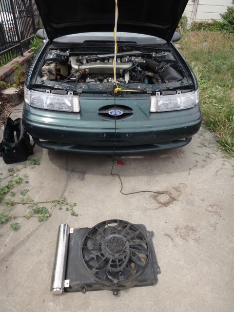 1995 Ford Taurus - Front view of a 1995 Ford Taurus with the hood open, showing the engine and a removed radiator fan.
