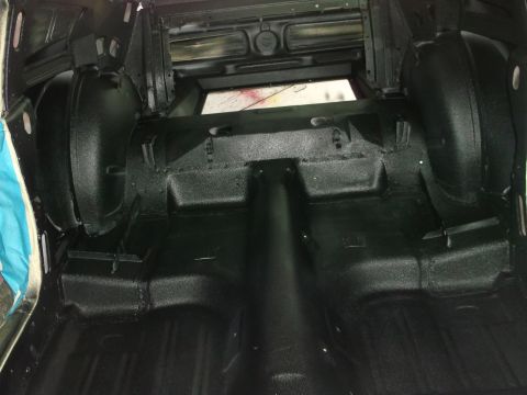 1967 Ford Mustang - The interior of a car trunk, showing the floor and wheel wells coated in black.