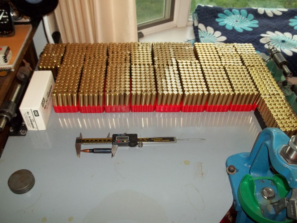 Lots of brass cartridges in red trays, a caliper measuring one cartridge, and a reloading press