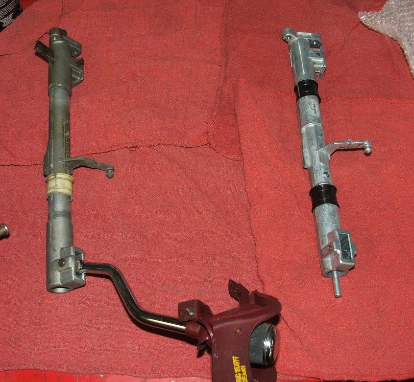 Two metal steering columns with linkages and black bands, laid on a red cloth