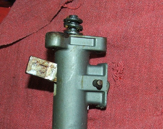 Close-up of a metal automotive part with a spring and a lever, on a red textured cloth