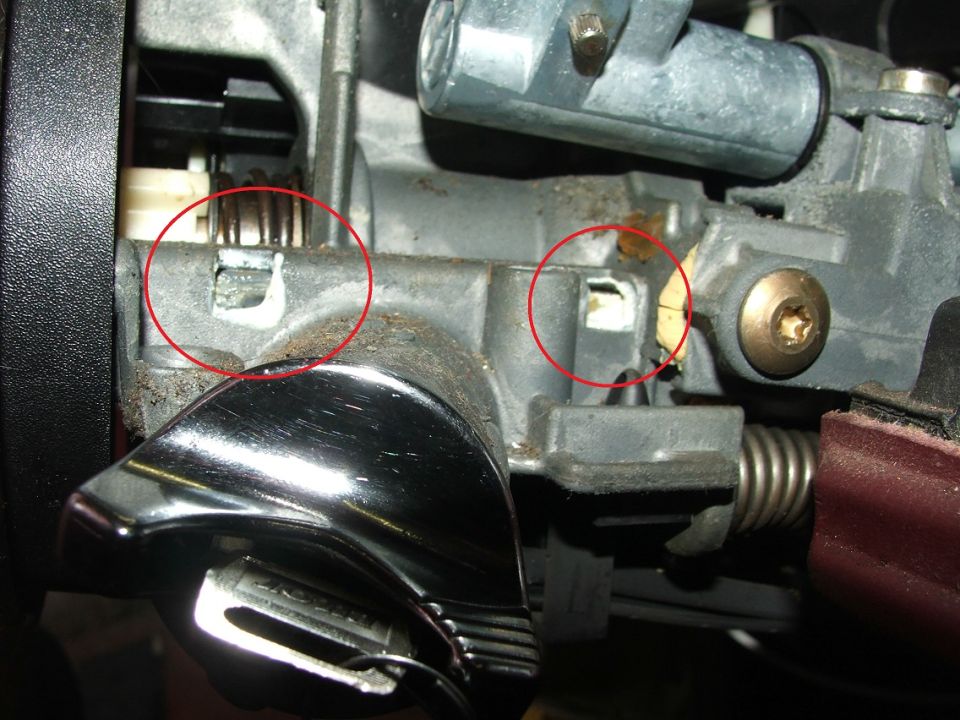 Close-up of automotive steering column mechanism with red circles highlighting internal components. A chrome lever is visible