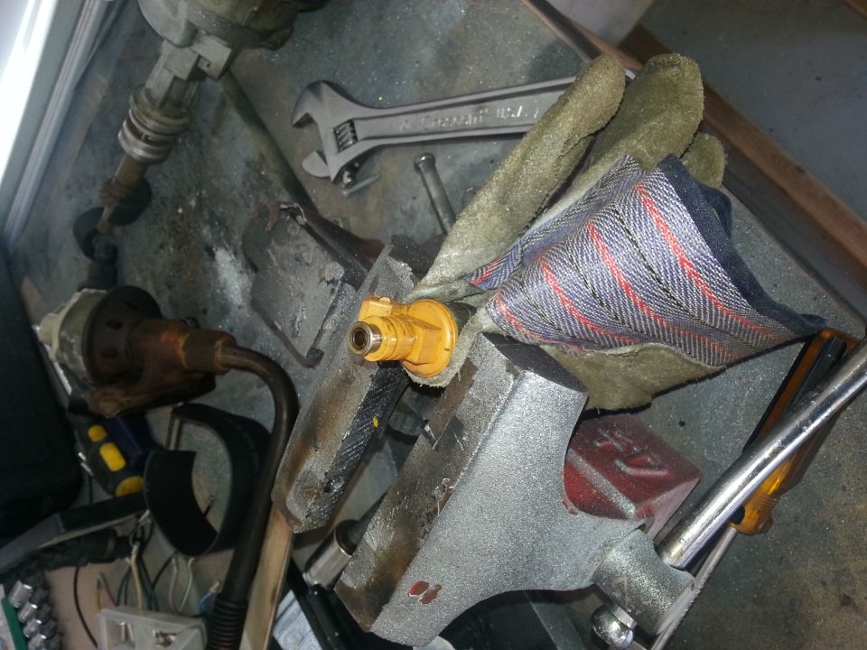 Yellow fuel injector held in a vise with a wrench and gloves nearby