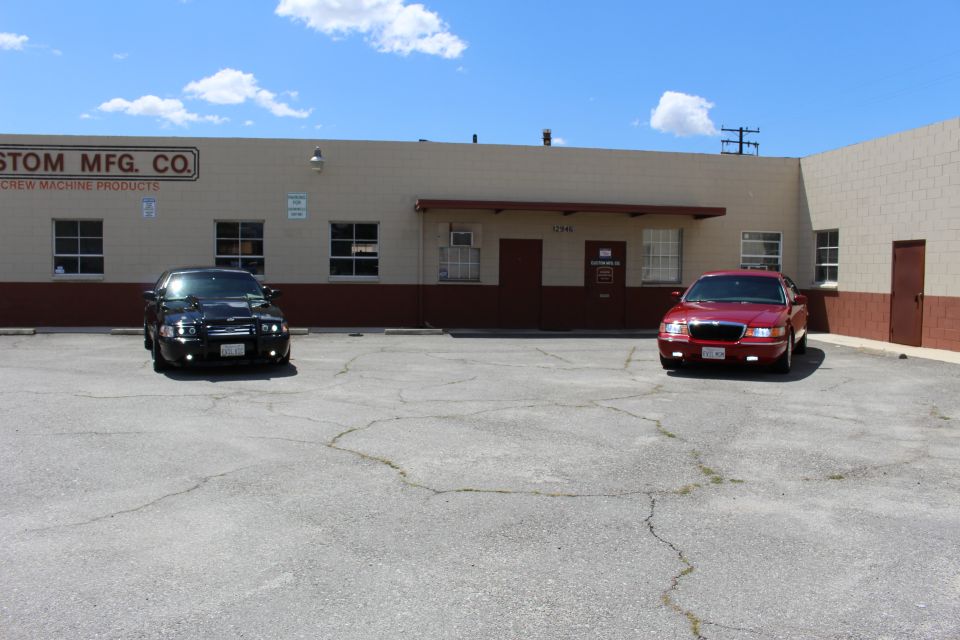 Black sedan and red sedan parked in a lot in front of a Custom Mfg Co building