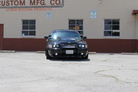 2003 Ford Crown Victoria - Head-on view of a lowered black Ford sedan with a brush guard and 'EVIL VIC' plate parked before a Custom Mfg. Co. building.