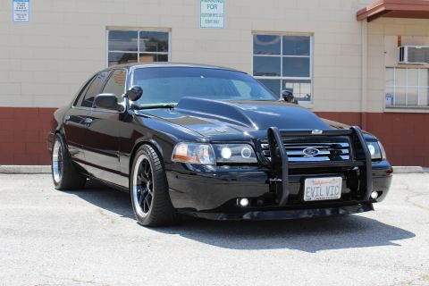 2003 Ford Crown Victoria - Front three-quarter view of a glossy black Ford Crown Victoria with a brush guard, polished-lip black wheels and an 'EVIL VIC' plate in fro…