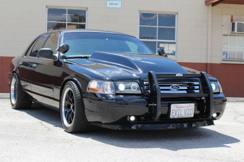 2003 Ford Crown Victoria - Close front view of a black Ford Crown Victoria fitted with a push bar holding an LED light bar and an 'EVIL VIC' California plate, parked…