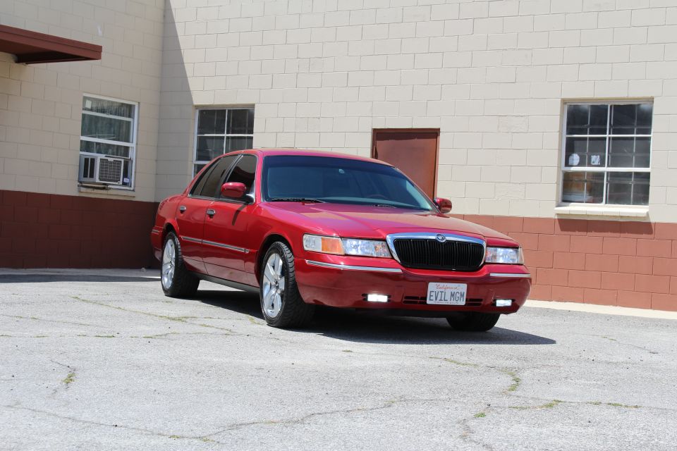 Red Mercury Grand Marquis sedan with EVIL MGM plate parked by a tan building