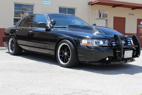 2003 Ford Crown Victoria - Low front three-quarter view of a black Ford Crown Victoria with a brush guard, red brake calipers and polished-lip black wheels in a paved…