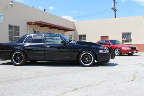 2003 Ford Crown Victoria - glossy black lowered Ford Crown Victoria sits in profile on black wheels with red calipers, a red Mercury sedan parked behind near an indus…