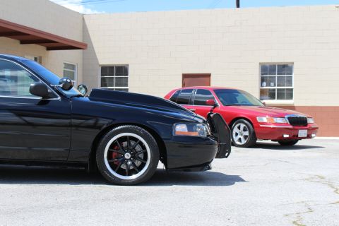 2003 Ford Crown Victoria - Close low view of a black Ford Crown Victoria's front fender and push bar with a red Mercury Grand Marquis parked alongside at an industria…