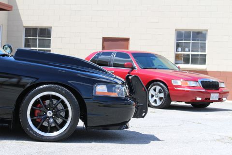 2003 Ford Crown Victoria - Low-angle shot of a black Ford Crown Victoria's polished-lip black wheel and fender, with a red Mercury Grand Marquis parked behind it.