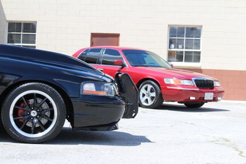 2003 Ford Crown Victoria - Low-angle view of a black Ford Crown Victoria's front wheel and headlight beside a red Mercury Grand Marquis showing its chrome grille and…