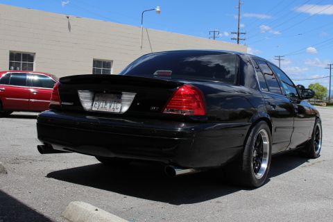 2003 Ford Crown Victoria - Rear view of a lowered black Ford Crown Victoria with a trunk spoiler, polished-lip black wheels and an 'EVIL VIC' plate, a red SUV parked…