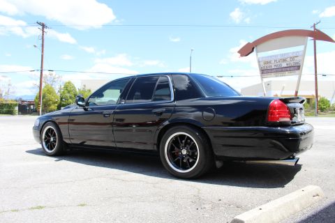 2003 Ford Crown Victoria - Rear three-quarter view of a lowered black Ford Crown Victoria with a trunk spoiler and black wheels parked beside a plating and welding sh…
