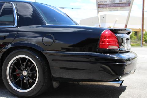 2003 Ford Crown Victoria - Close rear-quarter detail of a black Ford Crown Victoria showing its tail light, trunk spoiler, dual exhaust tip and polished-lip black whe…
