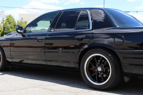 2003 Ford Crown Victoria - Side profile detail of a black Ford Crown Victoria showing the rear doors, chrome window trim and a polished-lip black wheel with red calip…