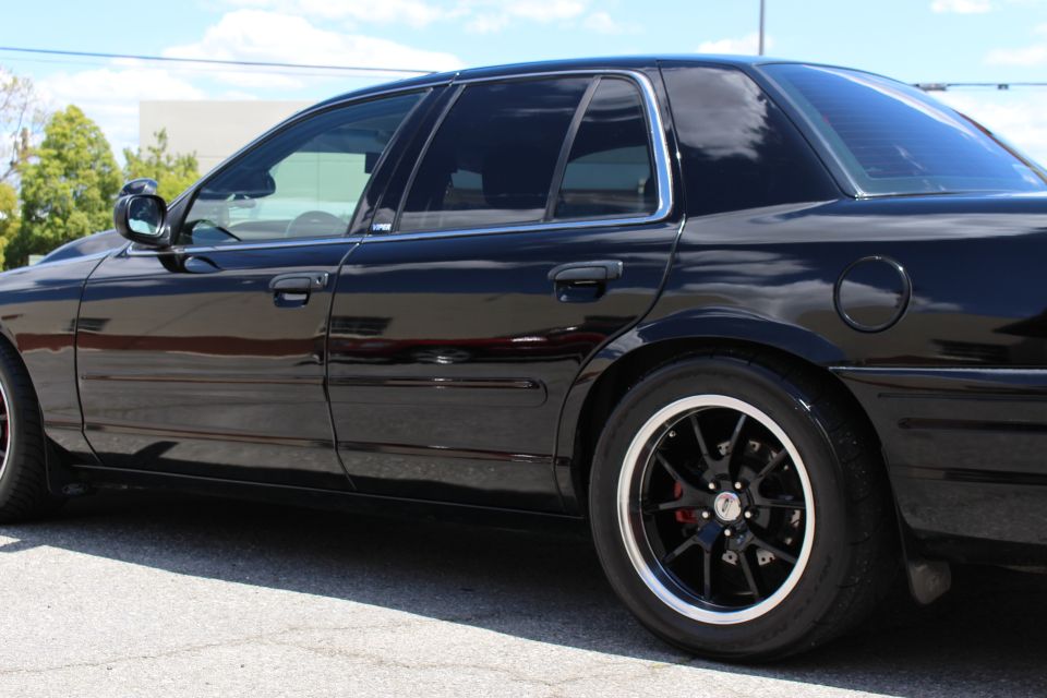 Side profile detail of a black sedan's rear door, pillar and black wheel